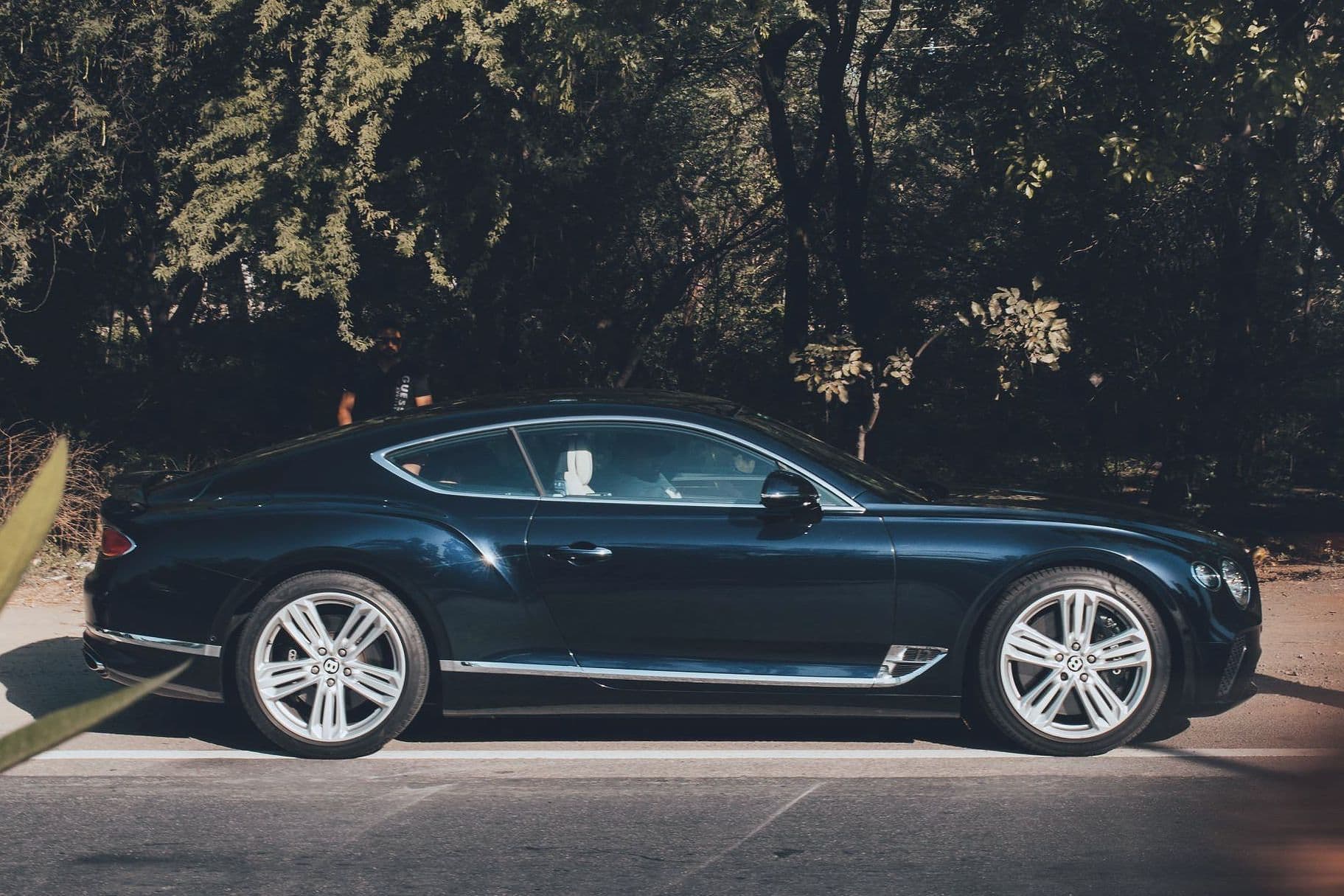 The dark blue Continental GT in profile on a tree-lined road.