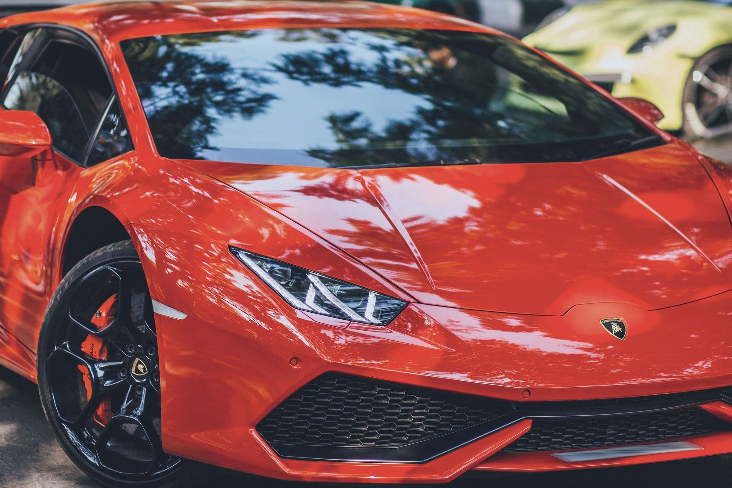 A red Lamborghini Huracán close up, front three-quarter, in dappled shade.