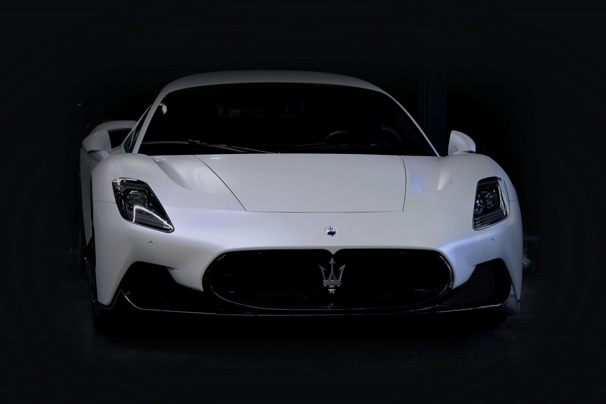A satin-white Maserati MC20 head-on in a dark garage.