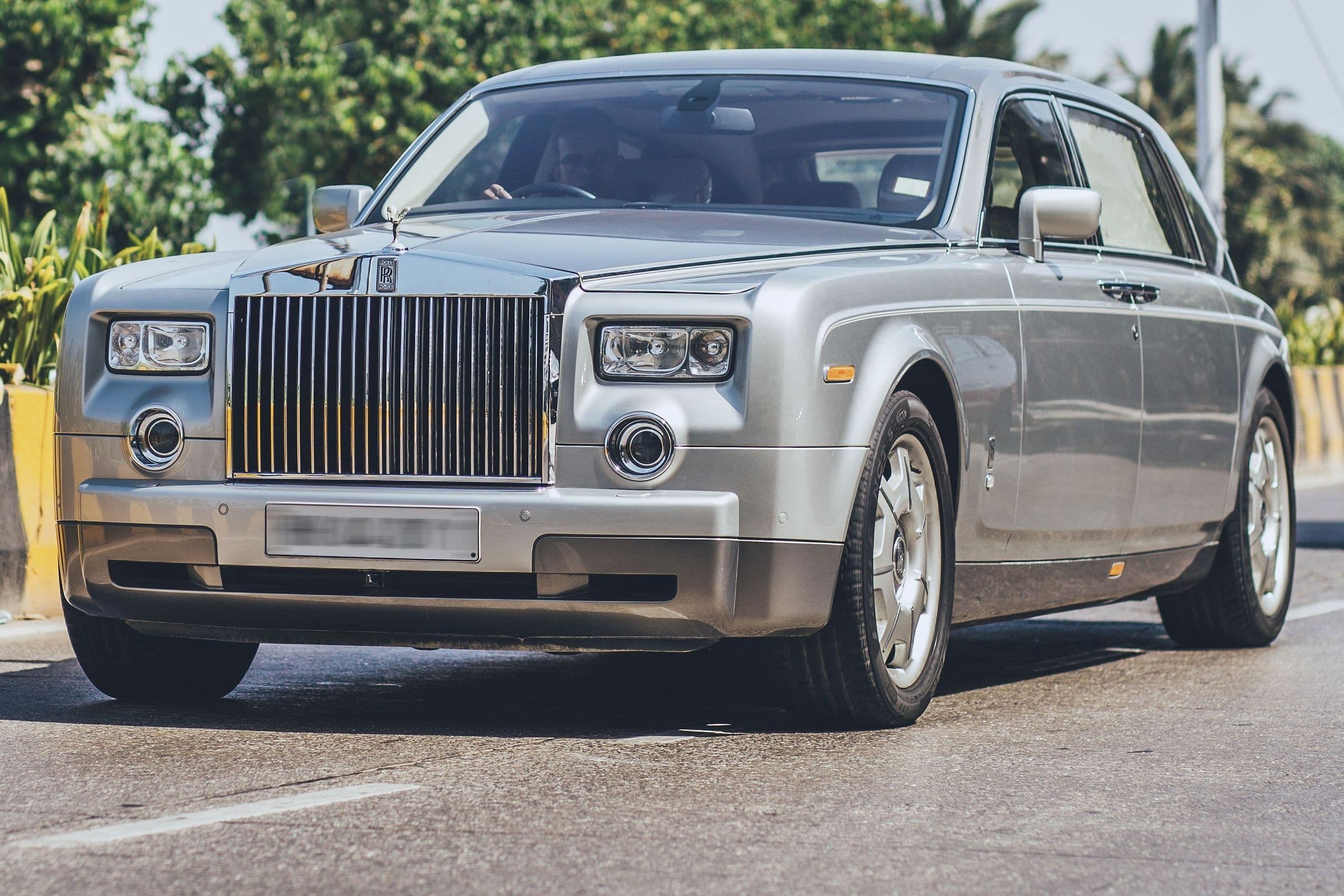 A silver Rolls-Royce Phantom on a sunlit road lined with palms.