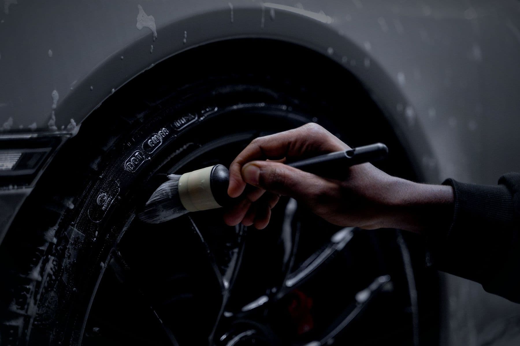 A hand brushing the 911's tyre sidewall during preparation.