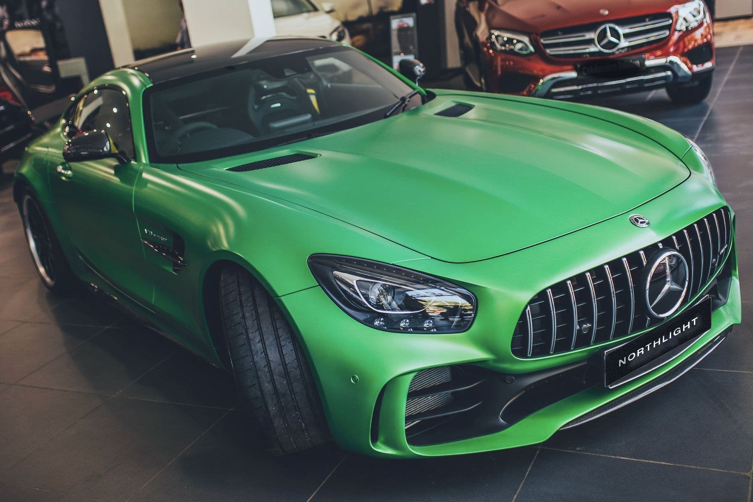 A matte green Mercedes-AMG GT R on a showroom floor, front three-quarter.