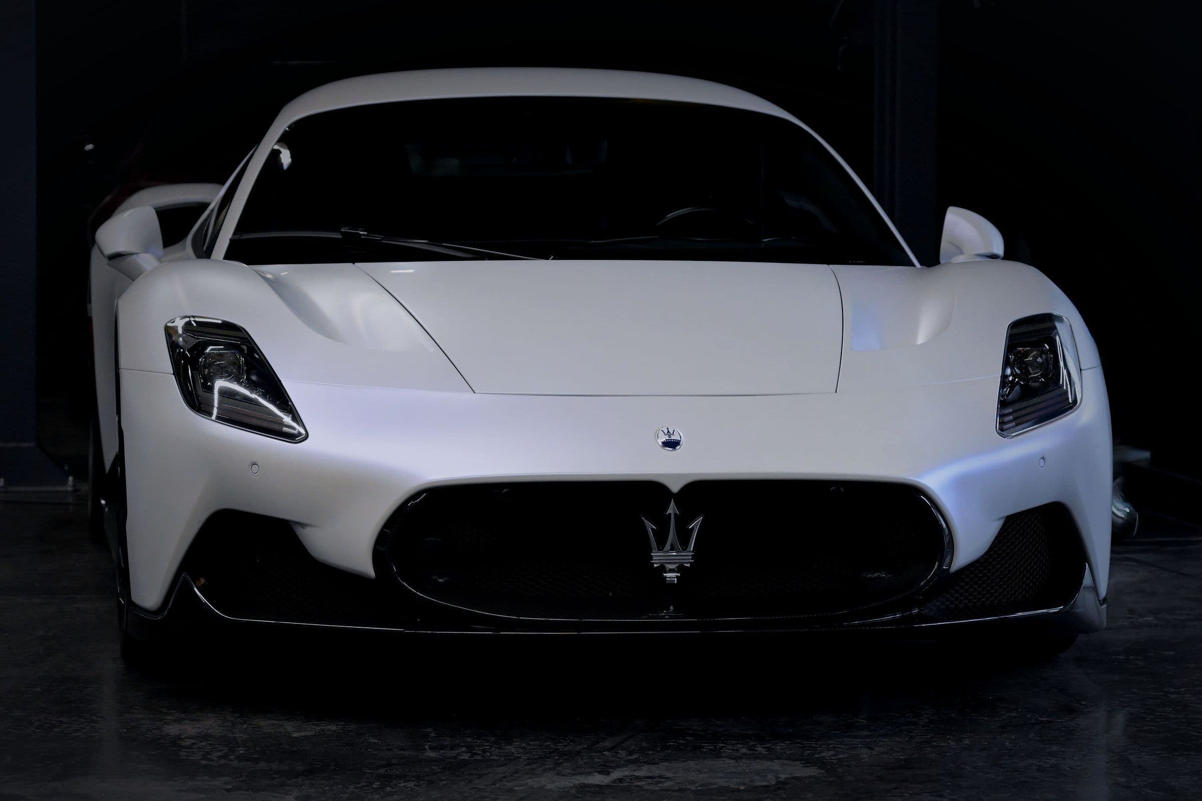 A satin-white Maserati MC20 head-on in a dark garage.